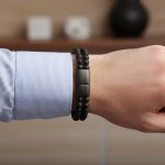Poignet d'un homme portant un bracelet en cuir tressé noir et perles de pierre de lave avec fermoir magnétique