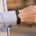 Poignet d'un homme portant un bracelet en cuir noir tressé et plat avec tube central en acier argenté et fermoir magnétique