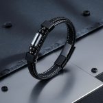 Bracelet homme en cuir noir et tube en acier argenté présenté sur ardoise et métal brossé