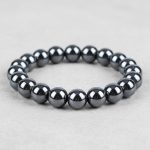 Gros plan d'un bracelet homme en perles d'hématite métallique brillante sur fond pierre claire avec 10mm de taille de perle