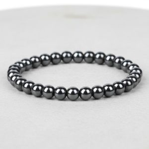 Gros plan d'un bracelet homme en perles d'hématite métallique brillante sur fond pierre claire avec 6 mm de taille de perle