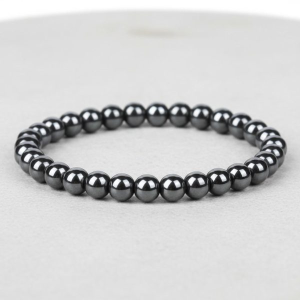 Gros plan d'un bracelet homme en perles d'hématite métallique brillante sur fond pierre claire avec 6 mm de taille de perle