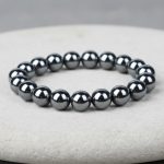 Gros plan d'un bracelet homme en perles d'hématite métallique brillante sur fond pierre claire avec 8 mm de taille de perle
