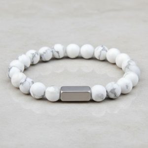 Gros plan d'un bracelet homme en perles de howlite blanche veinée de gris avec barre en acier brossé sur fond pierre claire