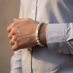 Poignet d'un homme portant un bracelet élastique en howlite blanche veinée avec barre centrale en acier brossé