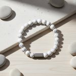 Bracelet homme en howlite blanche et barre en acier brossé présenté sur bois clair avec éléments naturels