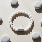 Bracelet homme en jade blanc et barre en acier brossé présenté sur bois clair avec éléments naturels