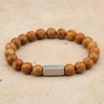 Gros plan d'un bracelet homme en perles de jaspe bois brun veiné avec barre en acier brossé sur fond pierre claire
