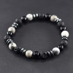 Gros plan d'un bracelet homme en jaspe paysage gris, onyx noir, pierre de lave et hématite sur fond ardoise