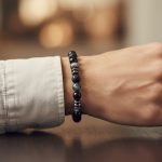 Poignet d'un homme portant un bracelet élastique en larvikite grise, onyx noir, pierre de lave et hématite