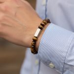 Poignet d'un homme portant un bracelet élastique en œil de tigre doré avec barre centrale en acier brossé