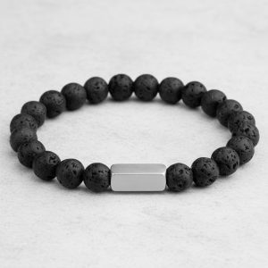 Gros plan d'un bracelet homme en perles de pierre de lave noire avec barre en acier brossé sur fond pierre claire