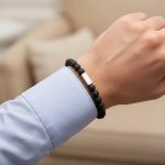Poignet d'un homme portant un bracelet élastique en pierre de lave noire avec barre centrale en acier brossé