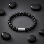 Bracelet homme en pierre de lave noire et barre en acier brossé présenté sur ardoise