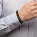 Poignet d'un homme portant un bracelet en cubes de pierre de lave tissé macramé avec cordon ajustable