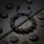 Bracelet homme en cubes de pierre de lave tissé macramé présenté sur ardoise et bois