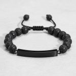 Gros plan d'un bracelet homme en perles de pierre de lave avec plaque en acier noir sur cordon ajustable