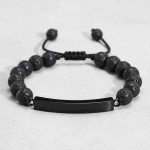Gros plan d'un bracelet homme en perles de pierre de lave avec plaque en acier noir sur cordon ajustable