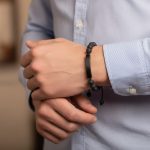 Poignet d'un homme portant un bracelet en perles de pierre de lave avec plaque centrale en acier noir et cordon ajustable