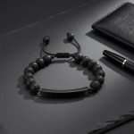 Bracelet homme en perles de pierre de lave et plaque en acier noir présenté sur ardoise