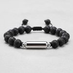 Gros plan d'un bracelet homme en perles de pierre de lave avec tube en acier argenté sur cordon ajustable
