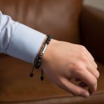 Poignet d'un homme portant un bracelet en perles de pierre de lave avec tube central en acier argenté et cordon ajustable