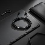Bracelet homme en perles de pierre de lave et tube en acier argenté présenté sur ardoise
