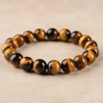 Gros plan d'un bracelet en grosses perles d'œil de tigre doré de 10 mm au reflet chatoyant sur fond pierre claire