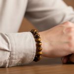 Poignet d'un homme portant un bracelet élastique en grosses perles d'œil de tigre doré de 10 mm
