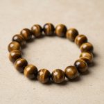 Gros plan d'un bracelet en grosses perles d'œil de tigre doré de 12 mm au reflet chatoyant sur fond pierre claire