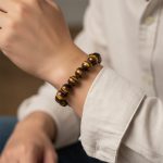 Poignet d'un homme portant un bracelet élastique en grosses perles d'œil de tigre doré de 12 mm