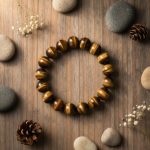Bracelet en grosses perles d'œil de tigre doré de 12 mm présenté sur bois avec éléments naturels