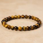 Gros plan d'un bracelet en perles fines d'œil de tigre doré de 6 mm sur fond pierre claire