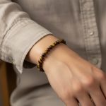 Poignet portant un bracelet élastique fin en perles d'œil de tigre doré de 6 mm