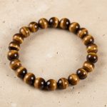 Gros plan d'un bracelet en perles d'œil de tigre doré de 8 mm au reflet chatoyant sur fond pierre claire