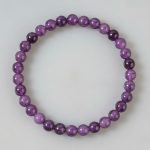 Gros plan d'un bracelet en perles fines d'améthyste violette de 6 mm sur fond clair
