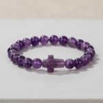 Gros plan d'un bracelet en perles d'améthyste violette avec croix sculptée en améthyste sur fond clair