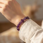 Poignet portant un bracelet élastique en perles d'améthyste violette avec croix centrale sculptée en améthyste