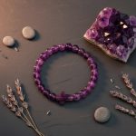 Bracelet en améthyste violette et croix sculptée présenté sur ardoise avec druse d'améthyste