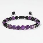 Gros plan d'un bracelet en améthyste violette facettée, onyx noir et séparateurs acier sur fond clair