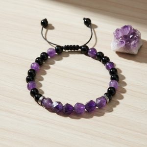 Bracelet en améthyste violette facettée, onyx et acier présenté sur pierre claire avec cristal d'améthyste