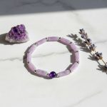 Bracelet en tubes d'améthyste lavande et perle d'améthyste foncée présenté sur pierre claire avec lavande séchée