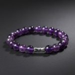 Gros plan d'un bracelet en perles d'améthyste violette avec perle tube gravée en acier sur fond sombre