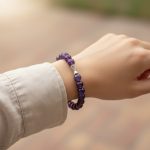 Poignet portant un bracelet élastique en améthyste violette avec perle centrale décorative en acier