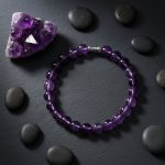 Bracelet en améthyste violette et perle en acier présenté sur ardoise avec druse d'améthyste