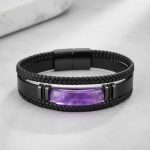 Gros plan d'un bracelet homme en cuir noir tressé avec barre en améthyste violette sur fond pierre claire