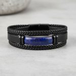 Gros plan d'un bracelet homme en cuir noir tressé avec barre en lapis-lazuli sur fond pierre claire