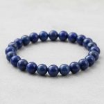 Gros plan d'un bracelet homme en perles de lapis-lazuli bleu moucheté de pyrite sur fond pierre claire