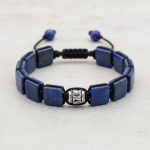 Gros plan d'un bracelet homme en plaques carrées de lapis-lazuli tissé macramé sur fond pierre claire