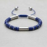 Gros plan d'un bracelet homme en rondelles de lapis-lazuli bleu et séparateurs acier sur fond pierre claire